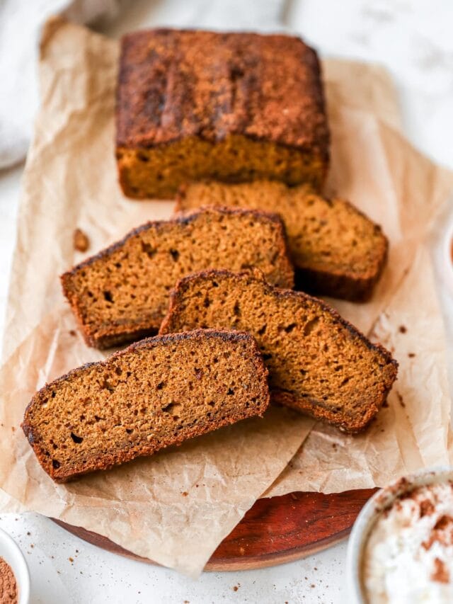 Four slices of pumpkin bread near the loaf of bread on parchment paper.