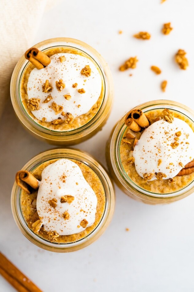 Overhead photo with three jars of pumpkin chia pudding with toppings including whipped coconut topping and granola.