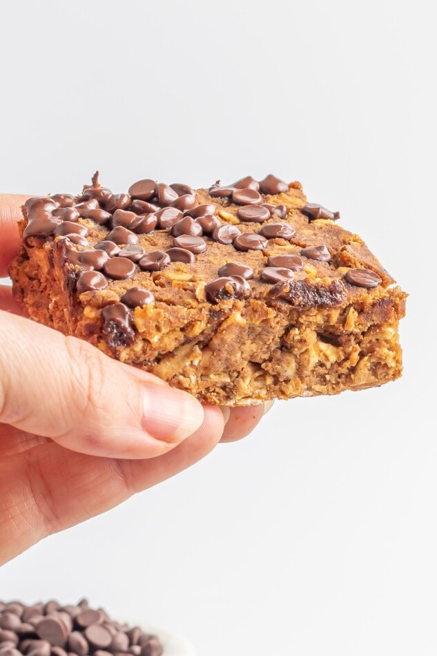 Save the recipe for these Vegan Protein Pumpkin Bars! A hand holding up a slice of pumpkin protein bars.