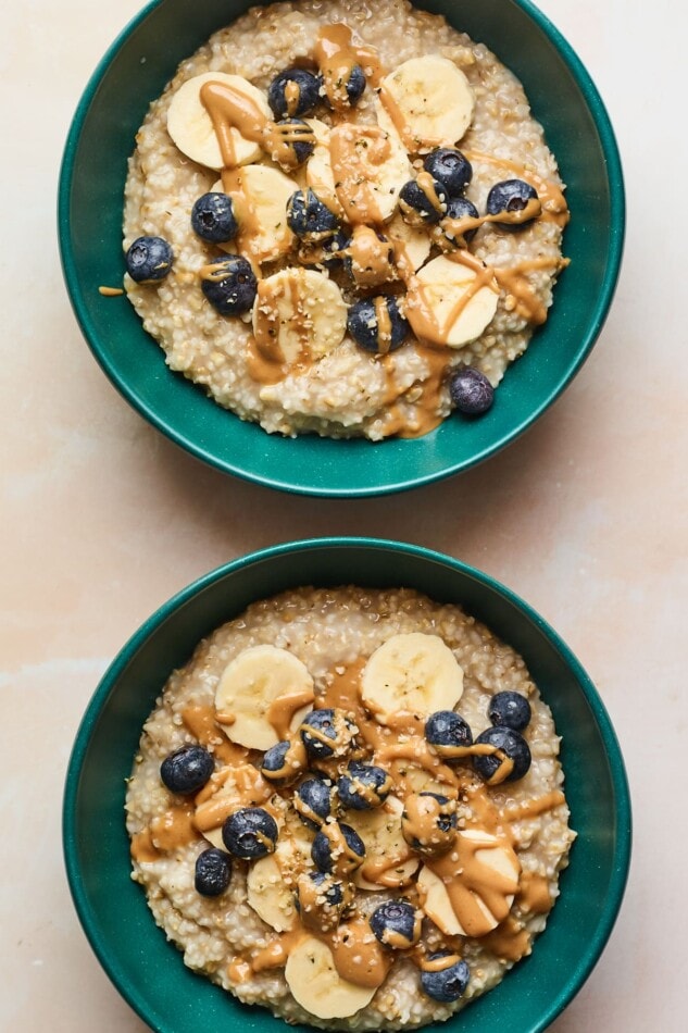 An overhead photo of two bowls of steel cut oatmeal with bananas, blueberries, and almond butter drizzled on top.