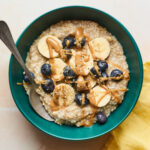 A serving of steel cut oats topped with banana slices, fresh blueberries, and a drizzle of almond butter.