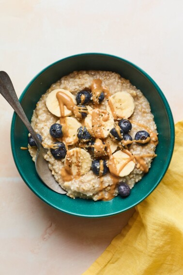 A serving of steel cut oats topped with banana slices, fresh blueberries, and a drizzle of almond butter.