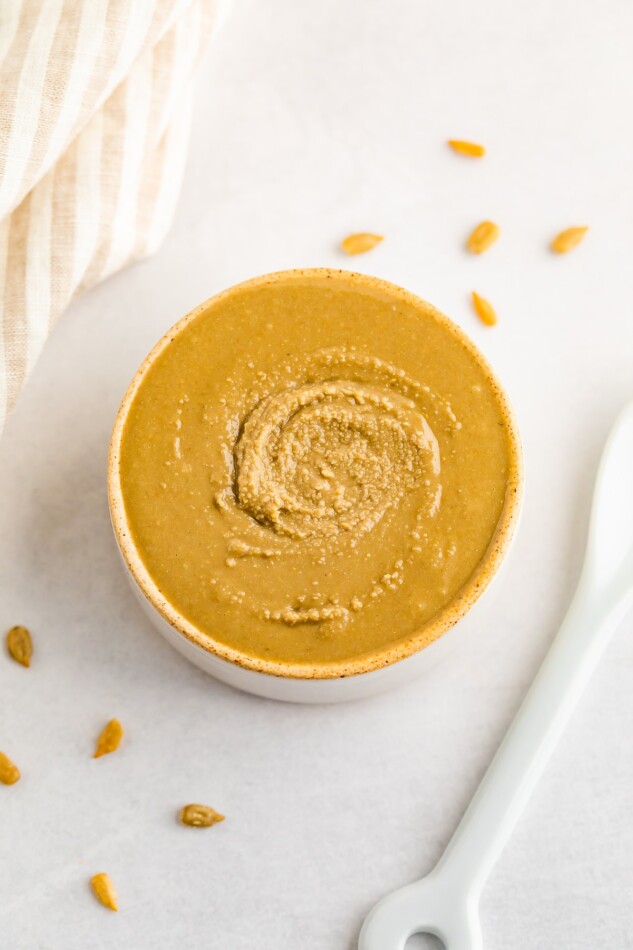 Overhead photo of sunflower butter in an open container with a spoon and some sunflower seeds scattered around.