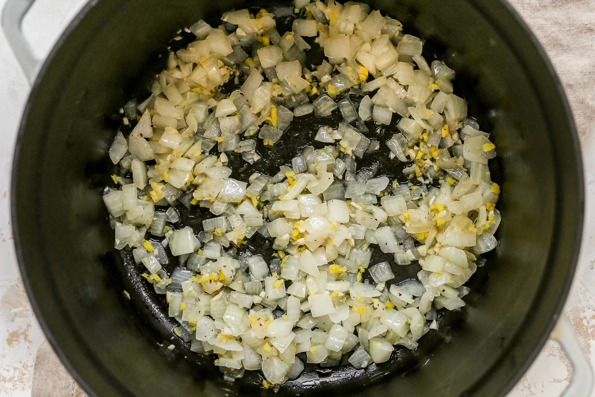 Overhead photo of onions, garlic, and spices in bottom of large pot.