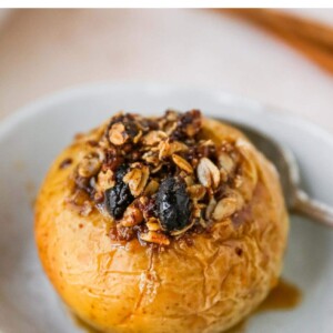 A baked apple with toppings served in a small dish with a silver spoon.