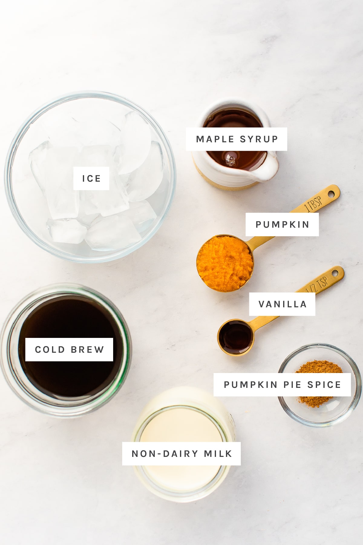 Ingredients measured out to make pumpkin cream cold brew: ice, maple syrup, pumpkin, vanilla, cold brew, pumpkin pie spice and non-dairy milk.