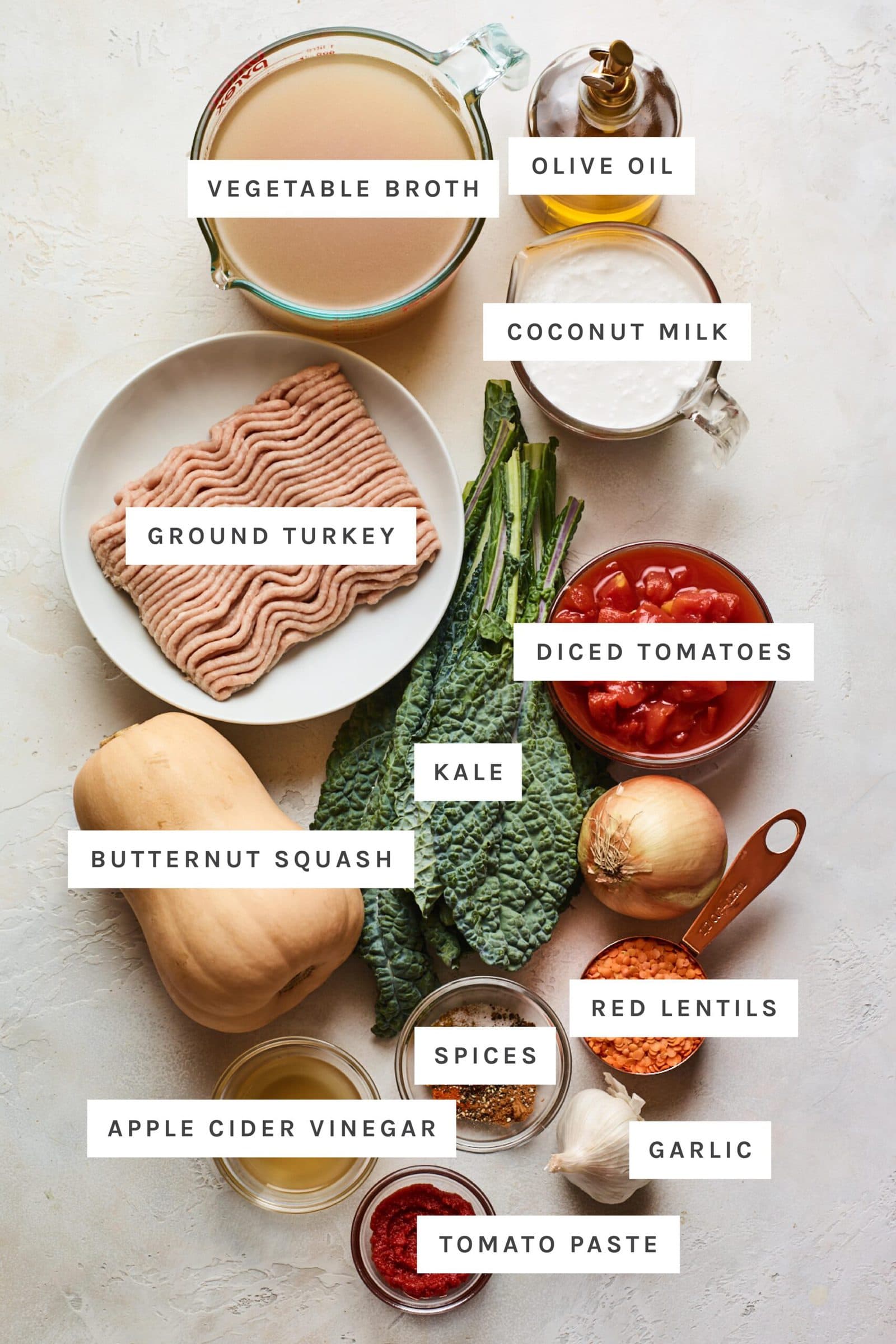 Ingredients measured out to make butternut squash turkey chili: vegetable broth, olive oil, coconut milk, ground turkey, diced tomatoes, kale, butternut squash, red lentils, spices, vinegar, garlic and tomato paste.