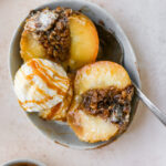 A baked apple in a bowl with a scoop of ice cream and a drizzle of caramel.