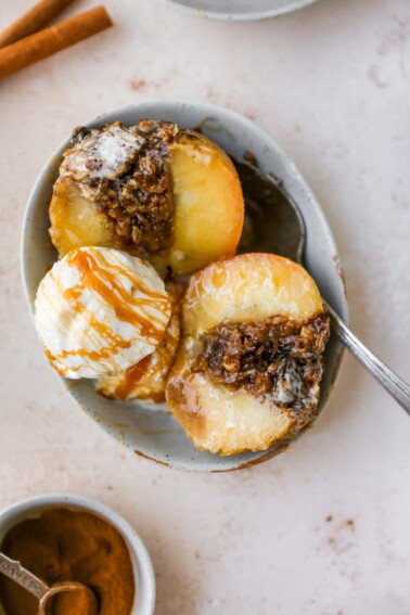 A baked apple in a bowl with a scoop of ice cream and a drizzle of caramel.