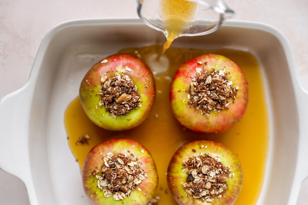 Warm apple drink poured into a rectangular baking dish holding 4 apples.