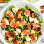 A serving of fig salad with arugula, figs, apple, goat cheese, and pecans.