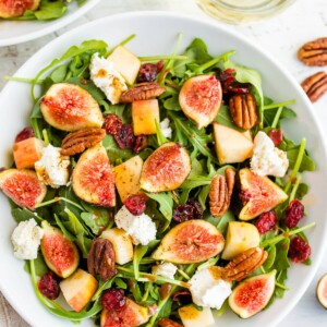 A serving of fig salad with arugula, figs, apple, goat cheese, and pecans.