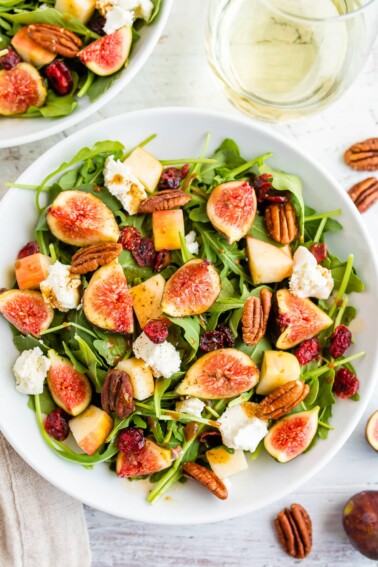 A serving of fig salad with arugula, figs, apple, goat cheese, and pecans.