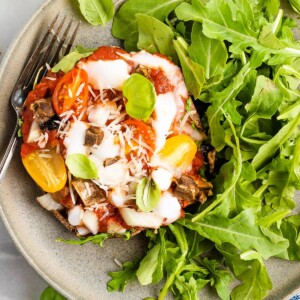 Portobello pizza on a plate with a serving of arugula salad to the side.