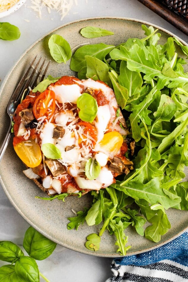 Close up, overhead photo of a portobello mushroom pizza plated with arugula. A silver fork rests on the plate.