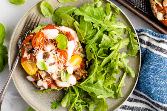 A serving of portobello mushroom pizza with an arugula salad to the side.