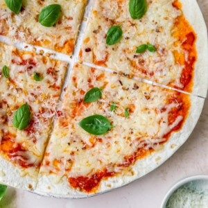 A tortilla pizza with melted cheese and topped with fresh basil leaves.