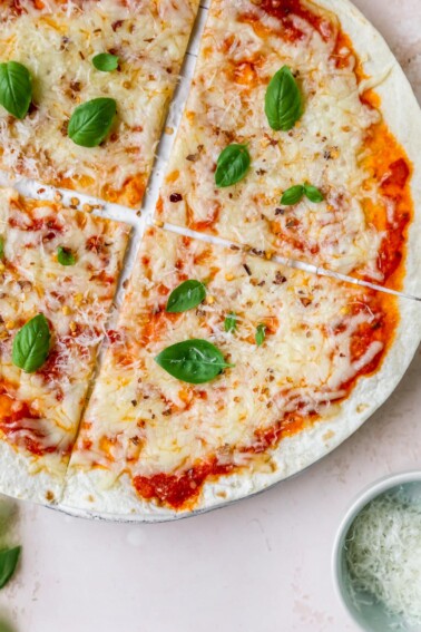 A tortilla pizza with melted cheese and topped with fresh basil leaves.