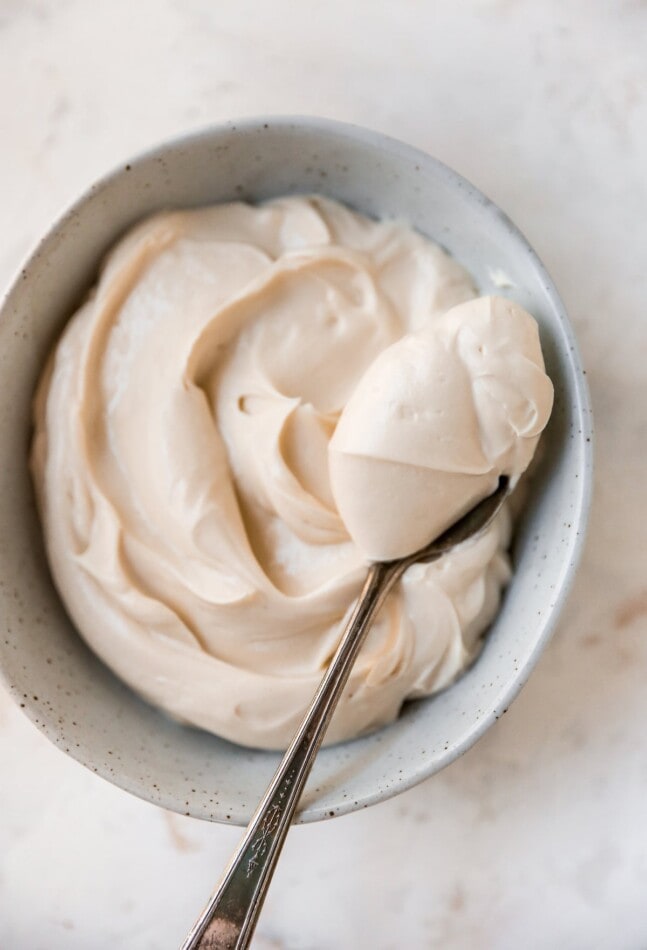 An overhead photo of a bowl of cream cheese frosting. A heaping spoonful is being held overtop of the bowl.