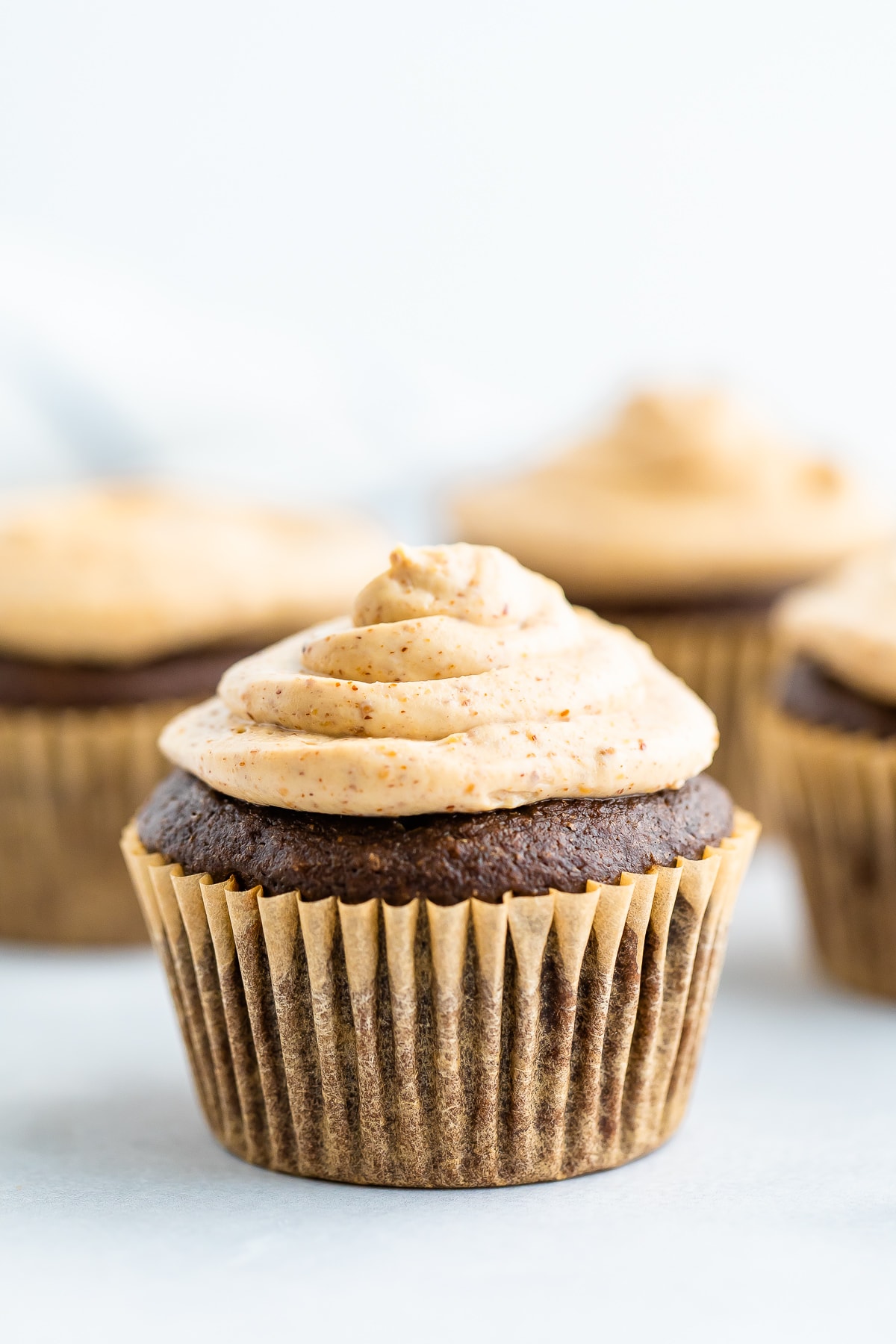 A chocolate cupcake in a brown wrapper topped with healthy greek yogurt frosting.