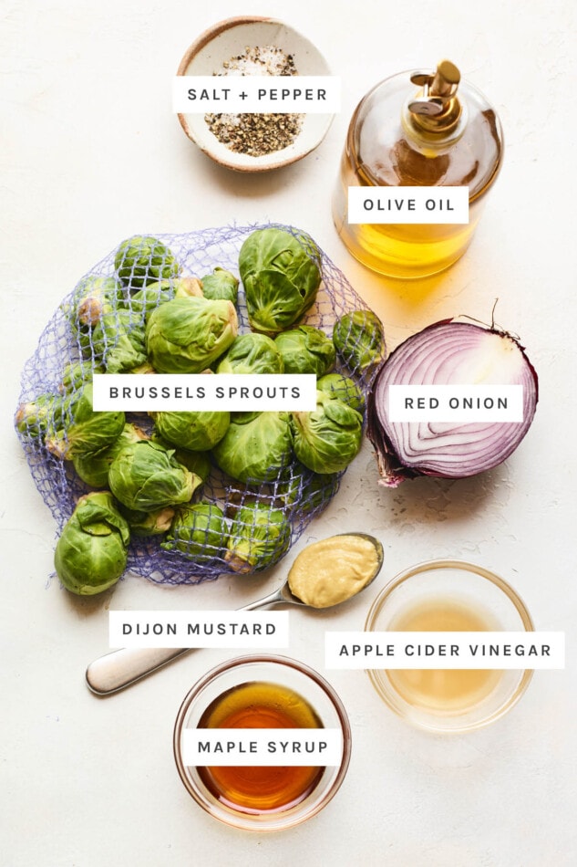 Brussels sprouts and red onion in a large white bowl with apple cider vinegar dressing. Ingredients measured out to make vinegar brussels sprouts: salt, pepper, olive oil, red onion, brussels sprouts, dijon mustard, apple cider vinegar and maple syrup.