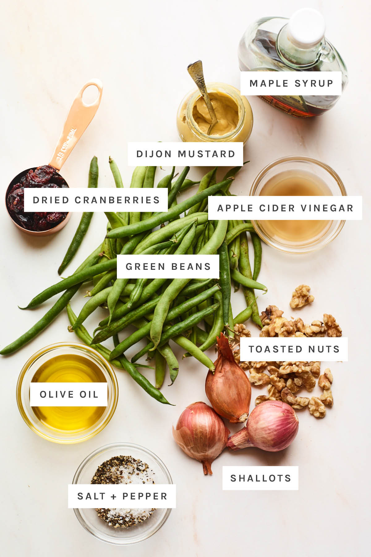 Ingredients measured out to make a green bean salad: maple syrup, dijon mustard, vinegar, dried cranberries, green beans, toasted nuts, olive oil, shallots, salt and pepper.