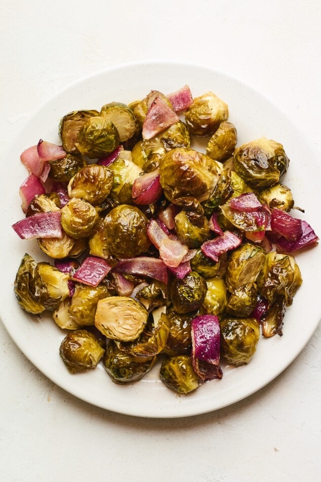 Roasted brussels sprouts and red onion on a large white plate.