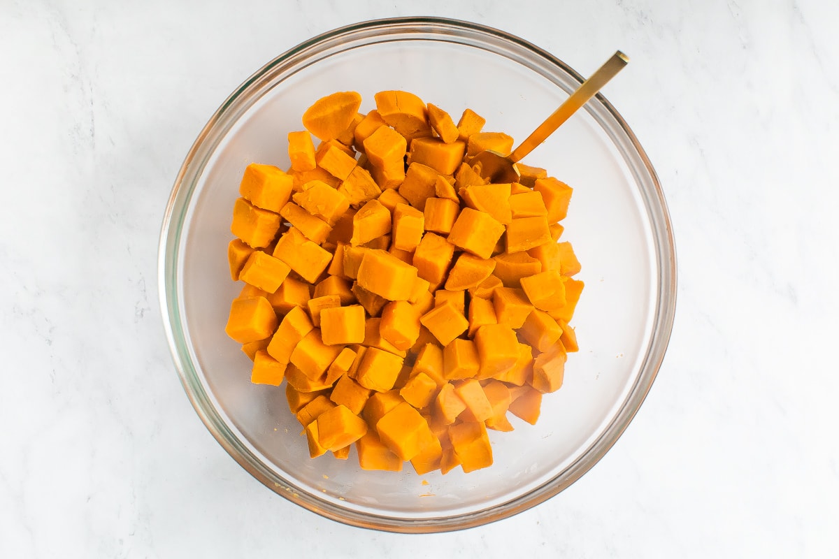 A glass mixing bowl containing sweet potato chopped into bite size pieces.