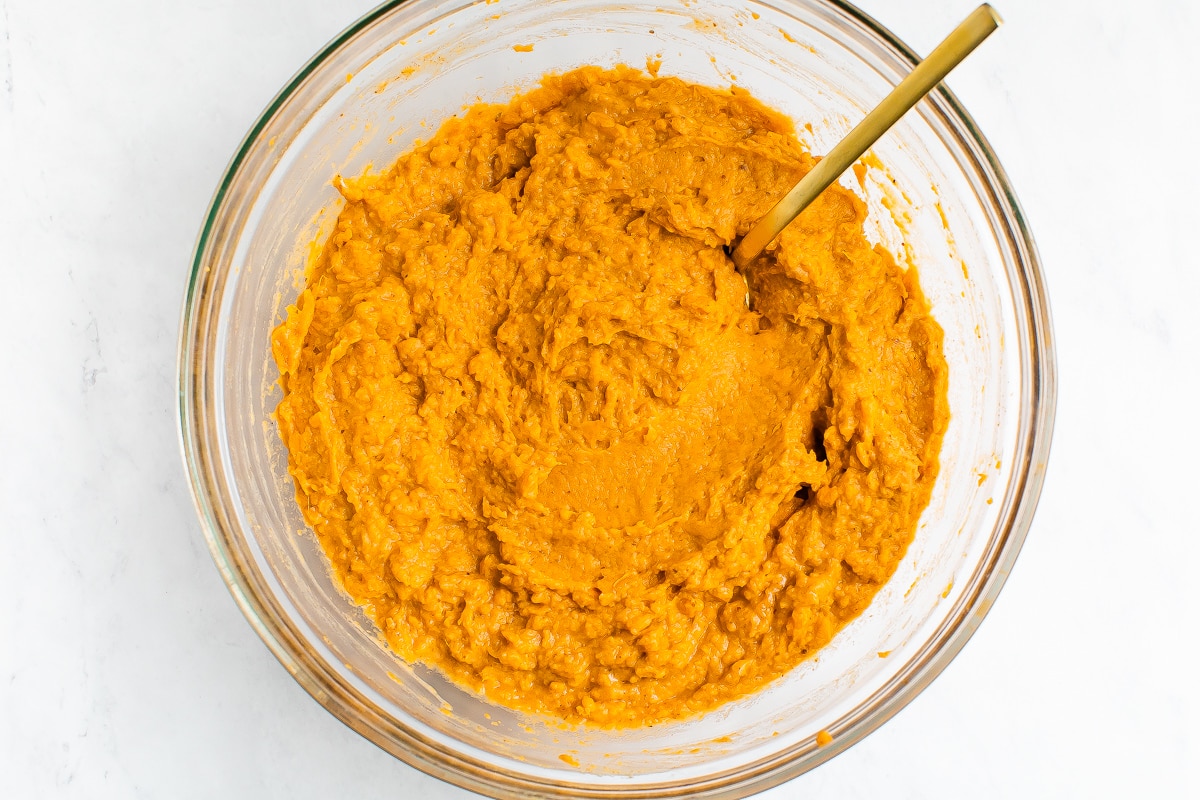 A mixing bowl containing mashed sweet potatoes. A fork rests inside the bowl.
