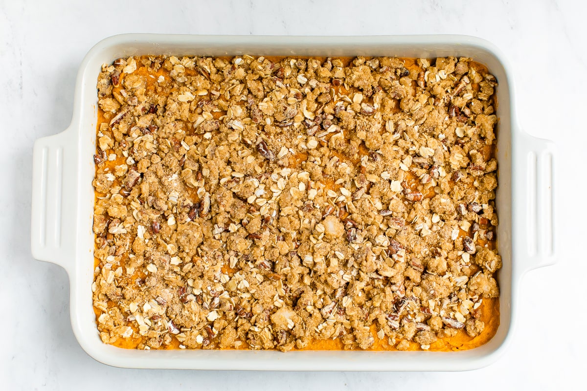 A ceramic baking dish containing mashed sweet potato, topped with an oat, pecan and brown sugar topping.