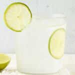 A drink glass containing vodka soda. A slice of lime is in the glass and another on the rim.