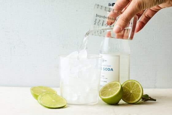 Vodka in a measuring cup being poured into a drinking glass filled with ice.