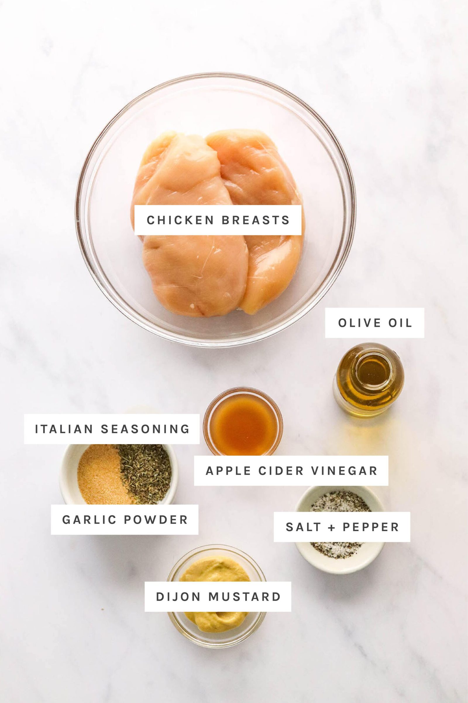 Ingredients measured out to make air fryer chicken breasts: olive oil, chicken breasts, Italian seasoning, garlic powder, vinegar, salt, pepper, and dijon mustard.