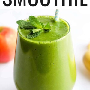 A glass containing green detox smoothie, topped with a fresh sprig of mint and with a striped straw.
