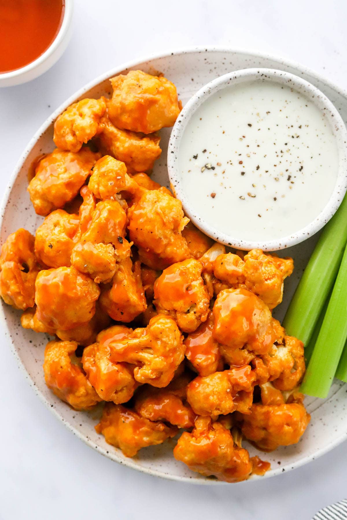 An overhead photo looking at a plate with air fryer buffalo cauliflower, celery sticks and a bowl of ranch for dipping.