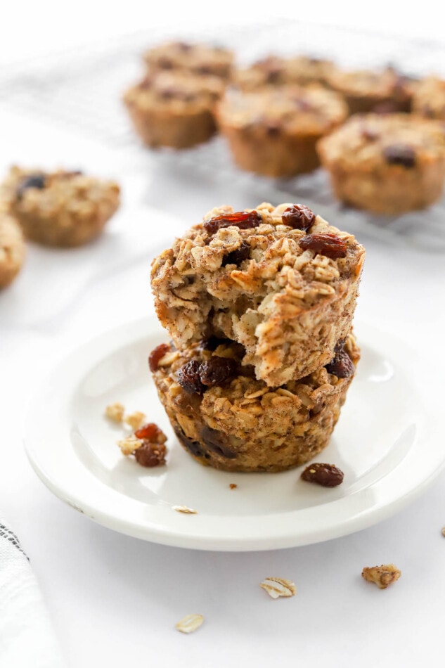 Baked Banana Oatmeal Cups Two banana baked oatmeal cups stacked on a small plate. The top oatmeal cup has a bite taken out of it.
