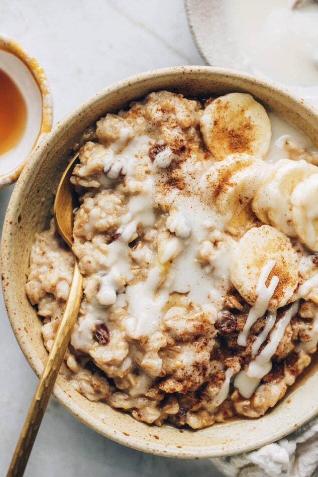 Ditch the instant oatmeal packets and make this Homemade Cinnamon Raisin Oatmeal -- it's healthier and takes less than 10 minutes to whip up! An overhead and closeup photo of a bowl of cinnamon raisin oatmeal topped with banana slices and a drizzle of coconut butter.