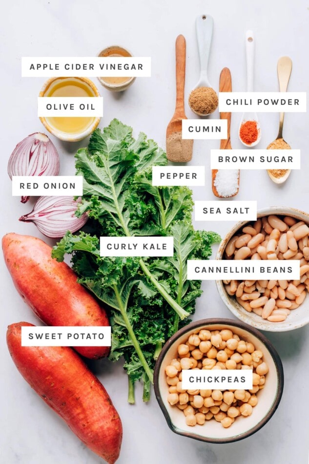 Ingredients measured out to make vegan power bowls: vinegar, pepper, cumin, chili powder, brown sugar, sea salt, olive oil, red onion, curly kale, cannellini beans, sweet potato and chickpeas.