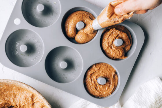 A hand using a pastry bag to pipe donut batter into the donut pan cavities.