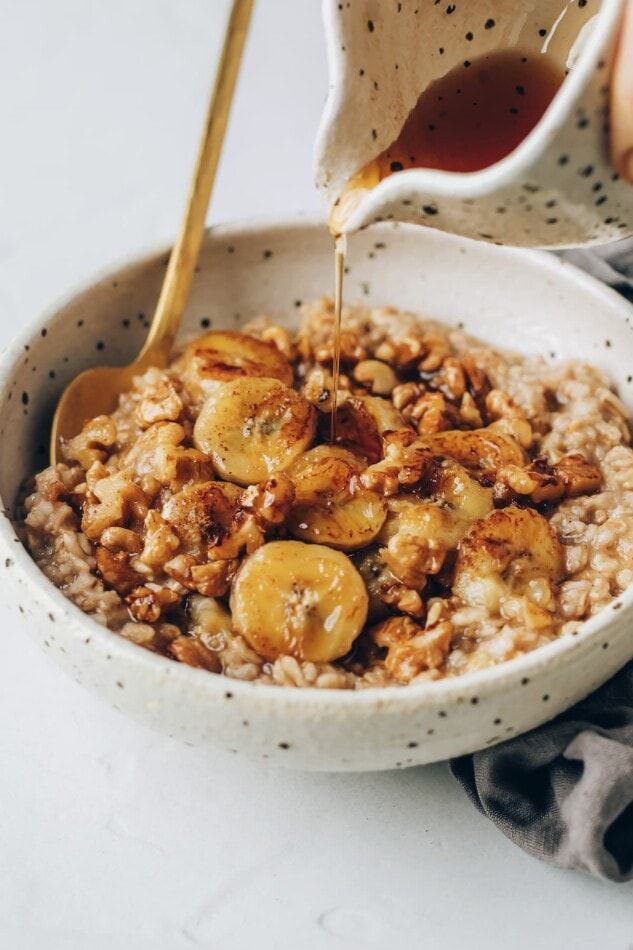 Caramelizing bananas and toasting walnuts in a small skillet. A bowl of banana bread oatmeal, topped with banana slices. A carafe is drizzling maple syrup over top of the oatmeal.