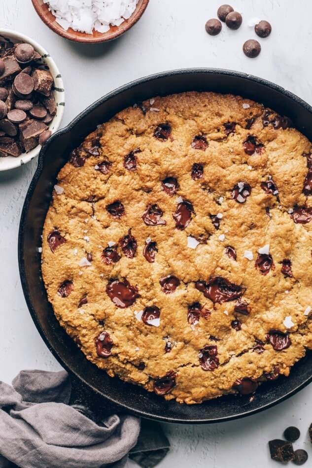 A cast iron skillet containing a baked chocolate chip cookie that encompasses the entire skillet.
