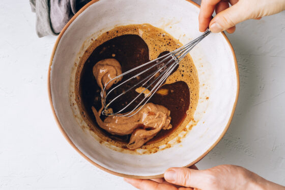 Coconut oil, almond butter, vanilla extract added to the egg and sugar mixture. The ingredients are being whisked together.