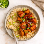 An overhead photo of a bowl of rice with healthy orange chicken. A fork rests in the rice.