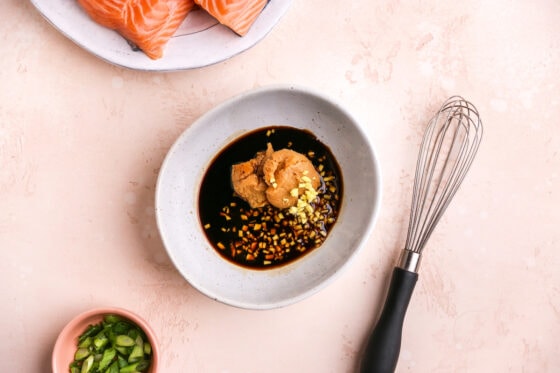 Miso, mirin, tamari and ginger in a small bowl. A whisk is next to the bowl to whisk the ingredients together.