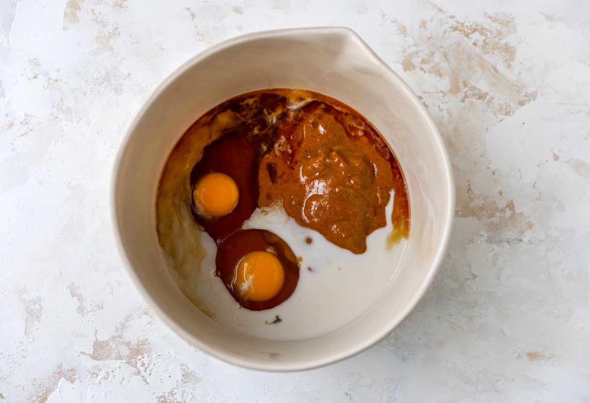 A cream mixing bowl containing almond butter, eggs, maple syrup, almond milk and vanilla extract.