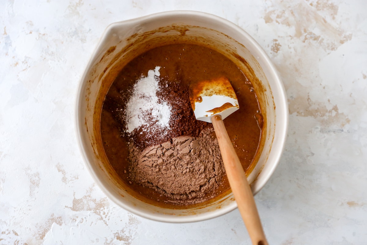 Protein powder, cocoa powder, sea salt and baking powder added to a cream mixing bowl with the wet ingredients.
