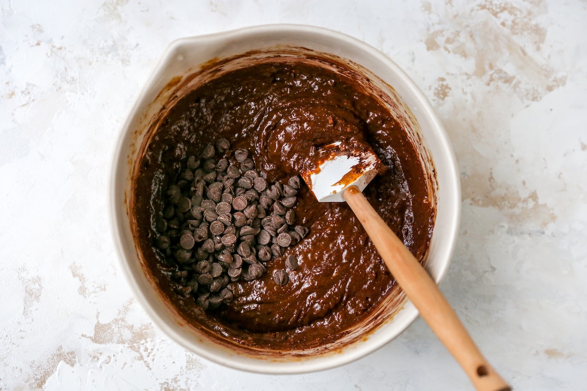 Chocolate chips added to the protein brownie batter. There is a white spatula in the bowl.