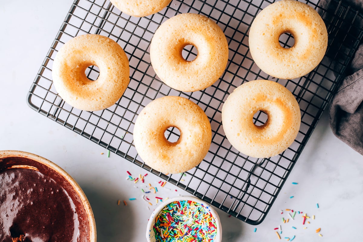 Multiple donuts on a cooling rack near a small bowl of colored sprinkles.