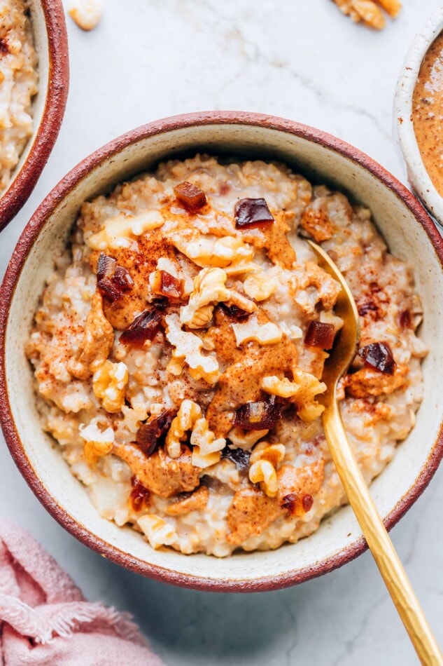 Pin this image to save the delicious recipe for Salted Date Oatmeal! An overhead photo of a bowl containing salted date nut oatmeal. A spoon rests in the bowl.