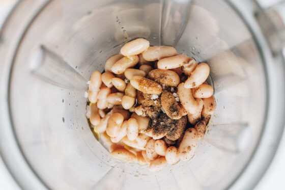 A high powered blender containing cannellini beans, water, vinegar, olive oil, salt, pepper and cumin.